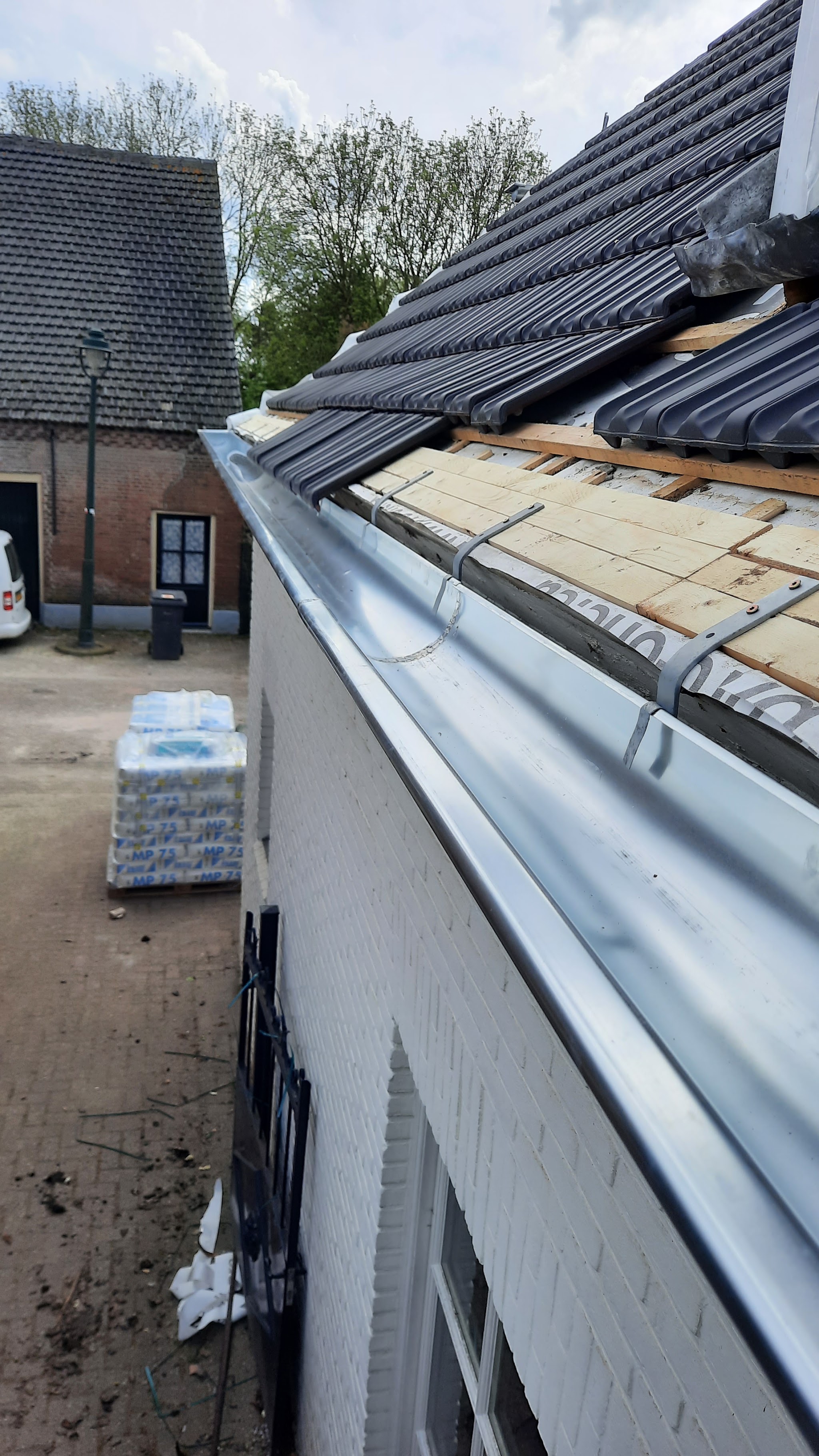 Nieuwe zinken goot langs de rand van een pannendak boven een witte gevel