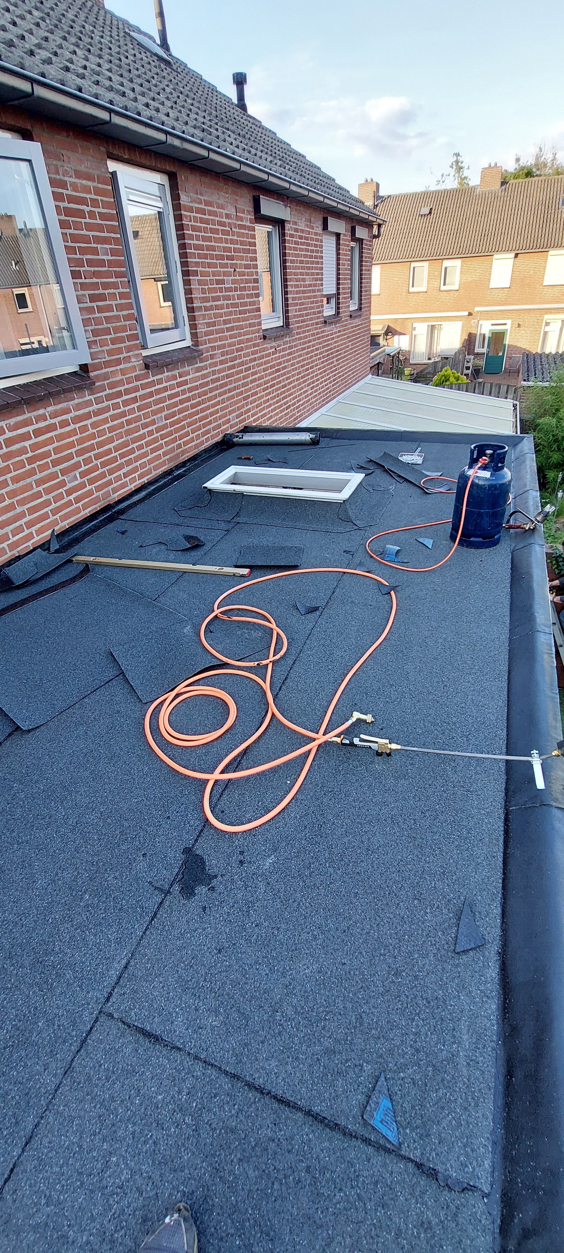 Nieuwe zwarte bitumen dakbedekking op een aanbouw met dakraam, gasfles en brander op het dak